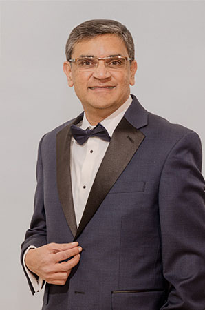 A man wearing a tuxedo with a bow tie stands confidently next to a wall with text.